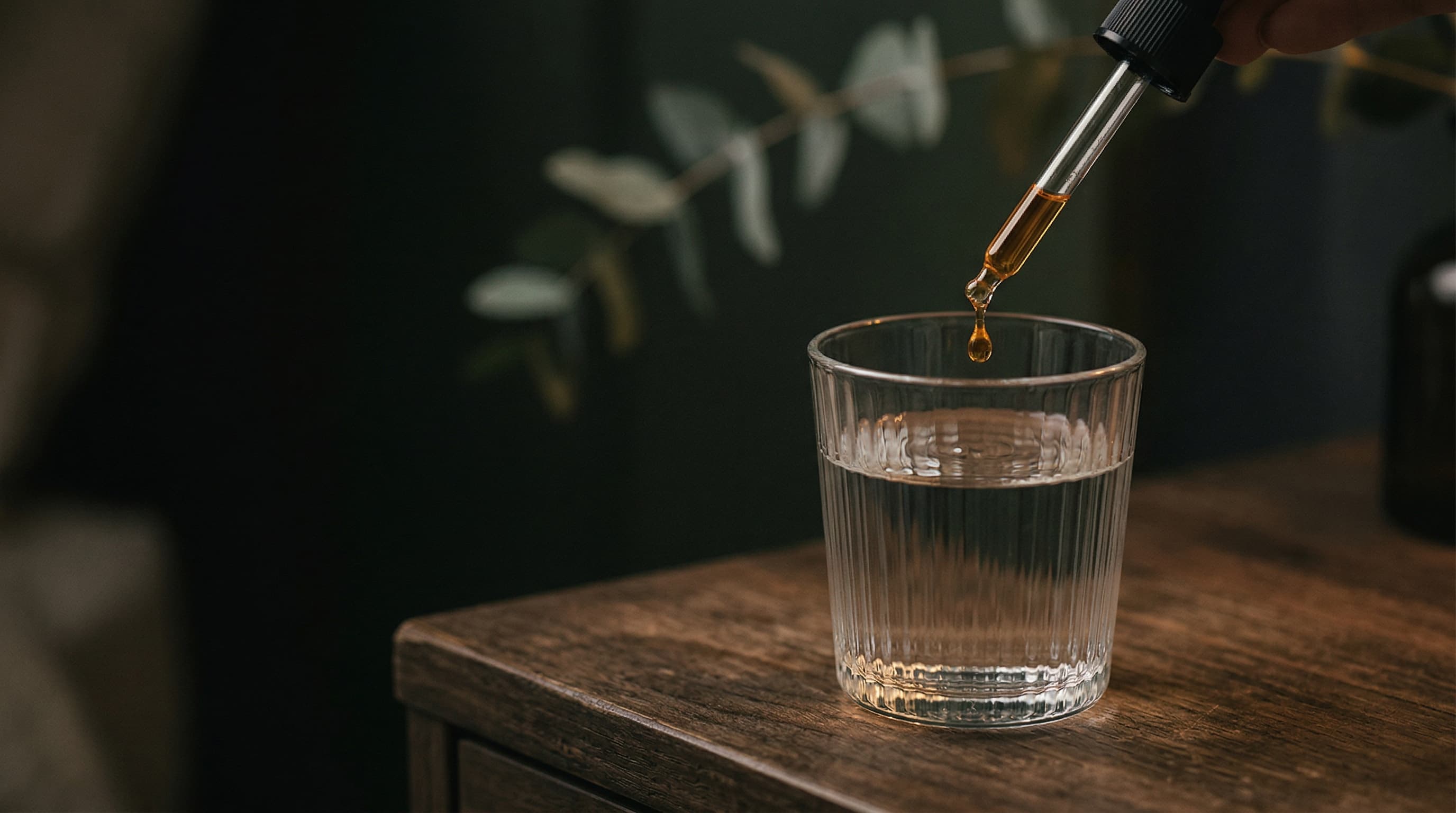 CBN oil dropper being held over a glass of water at nighttime